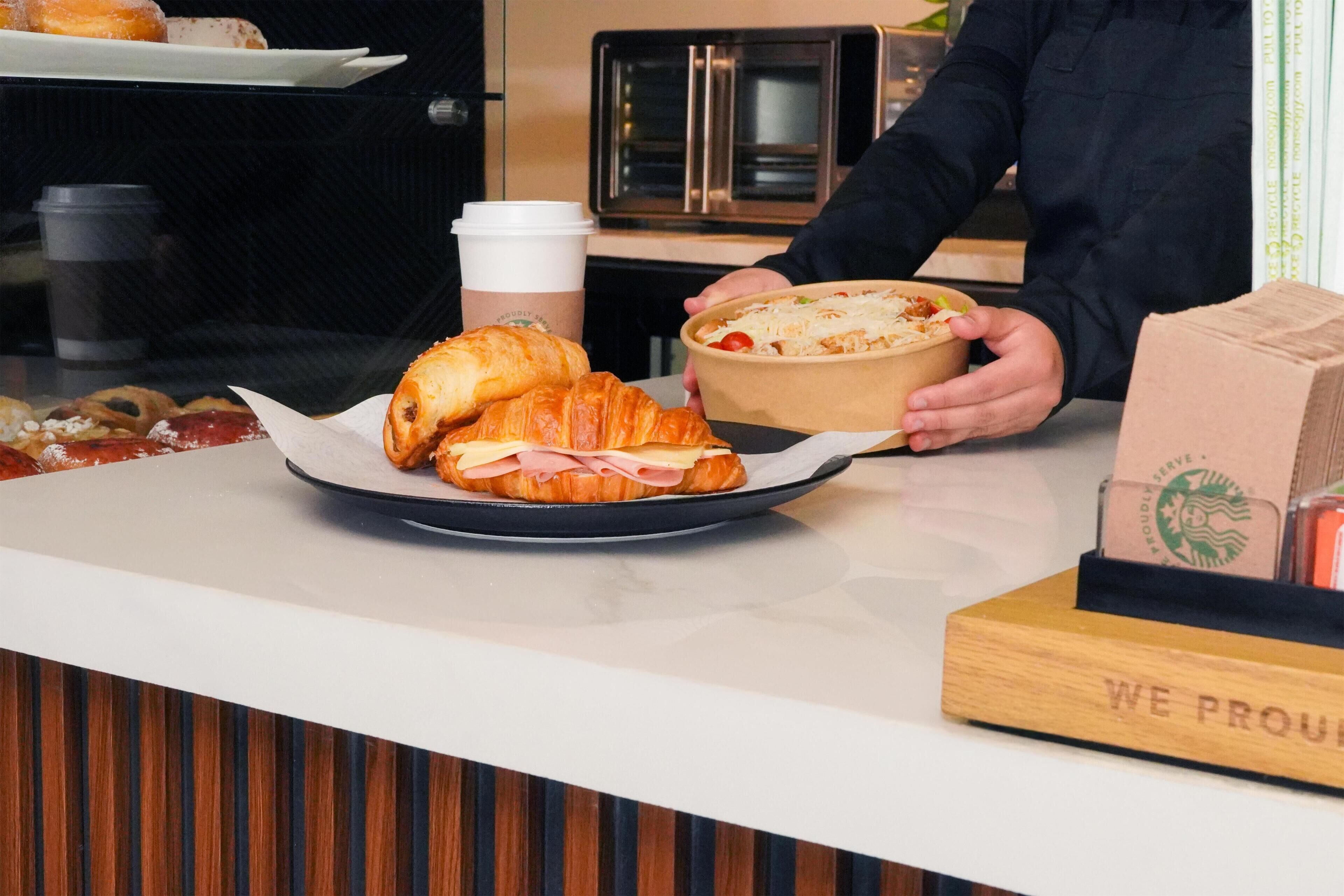 A counter with a plate of croissants and a container of food, a coffee cup, and a Starbucks branded box.