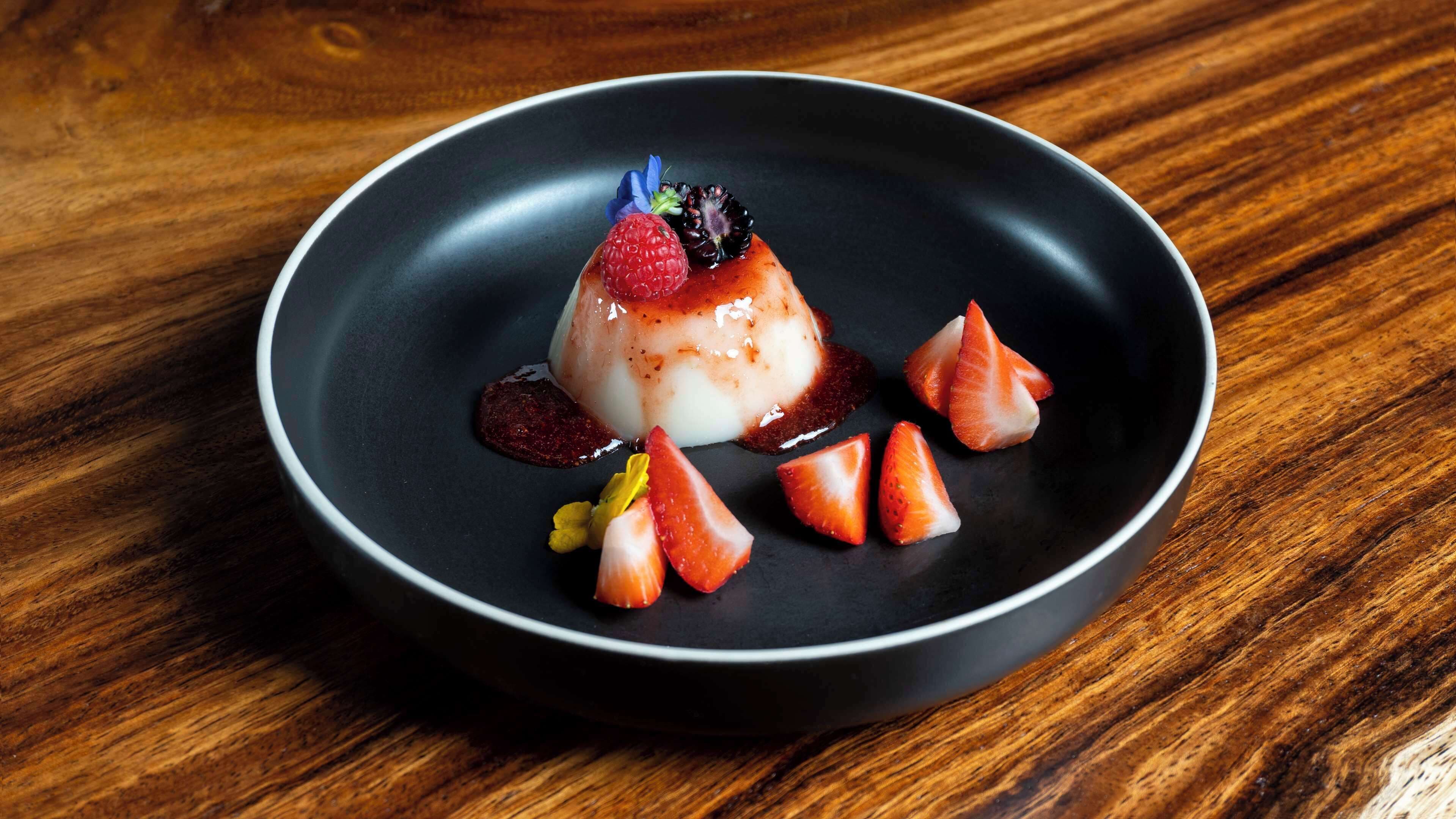 A dessert on a black plate with strawberries and a berry on top.