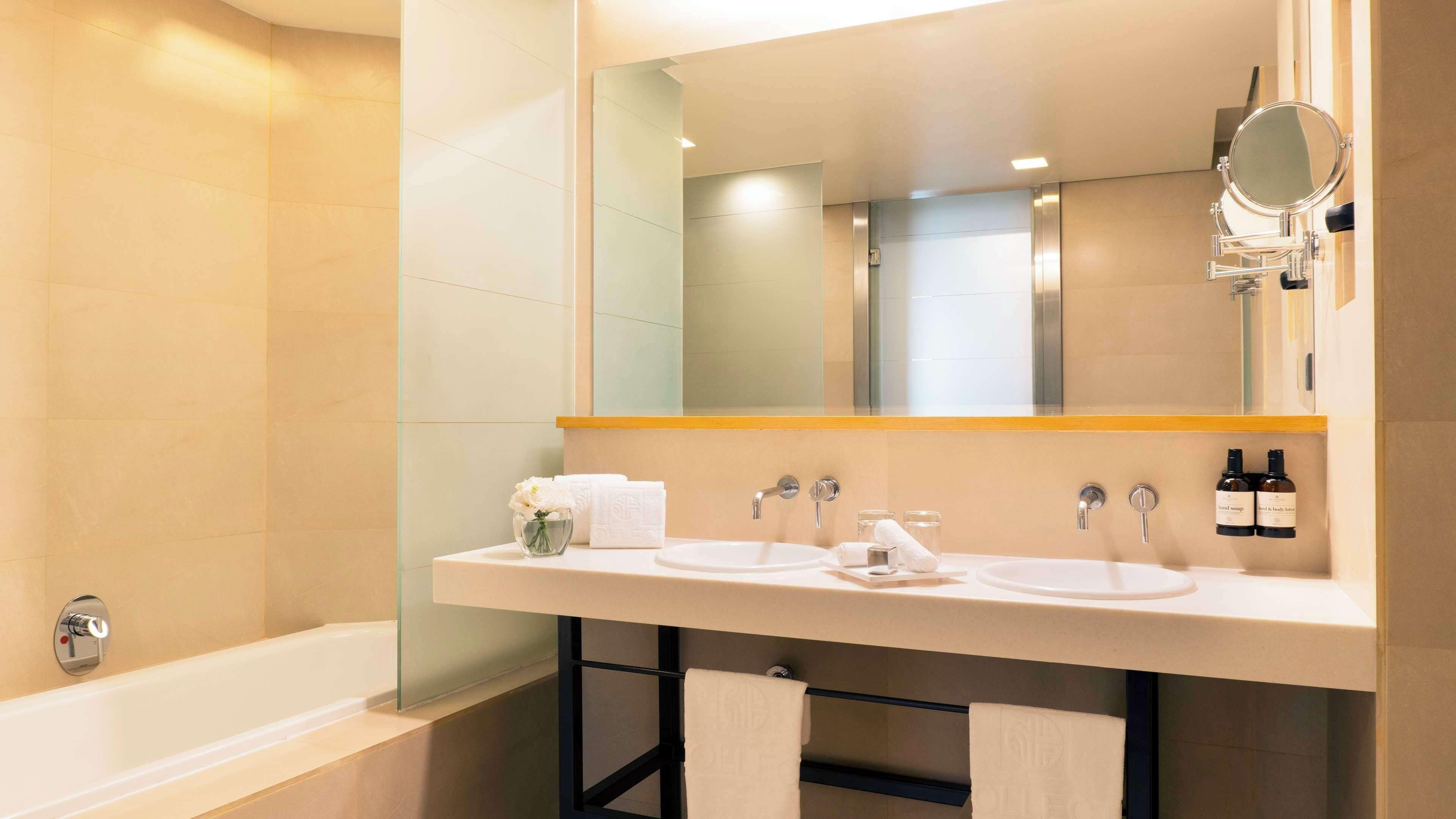 A modern bathroom with a double sink, a large mirror, and a bathtub.