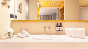 A hotel bathroom with a white sink, two bottles of hand soap, a mirror, and a vase with white flowers. - NH Collection Mexico City Airport T2 (Mexico City)