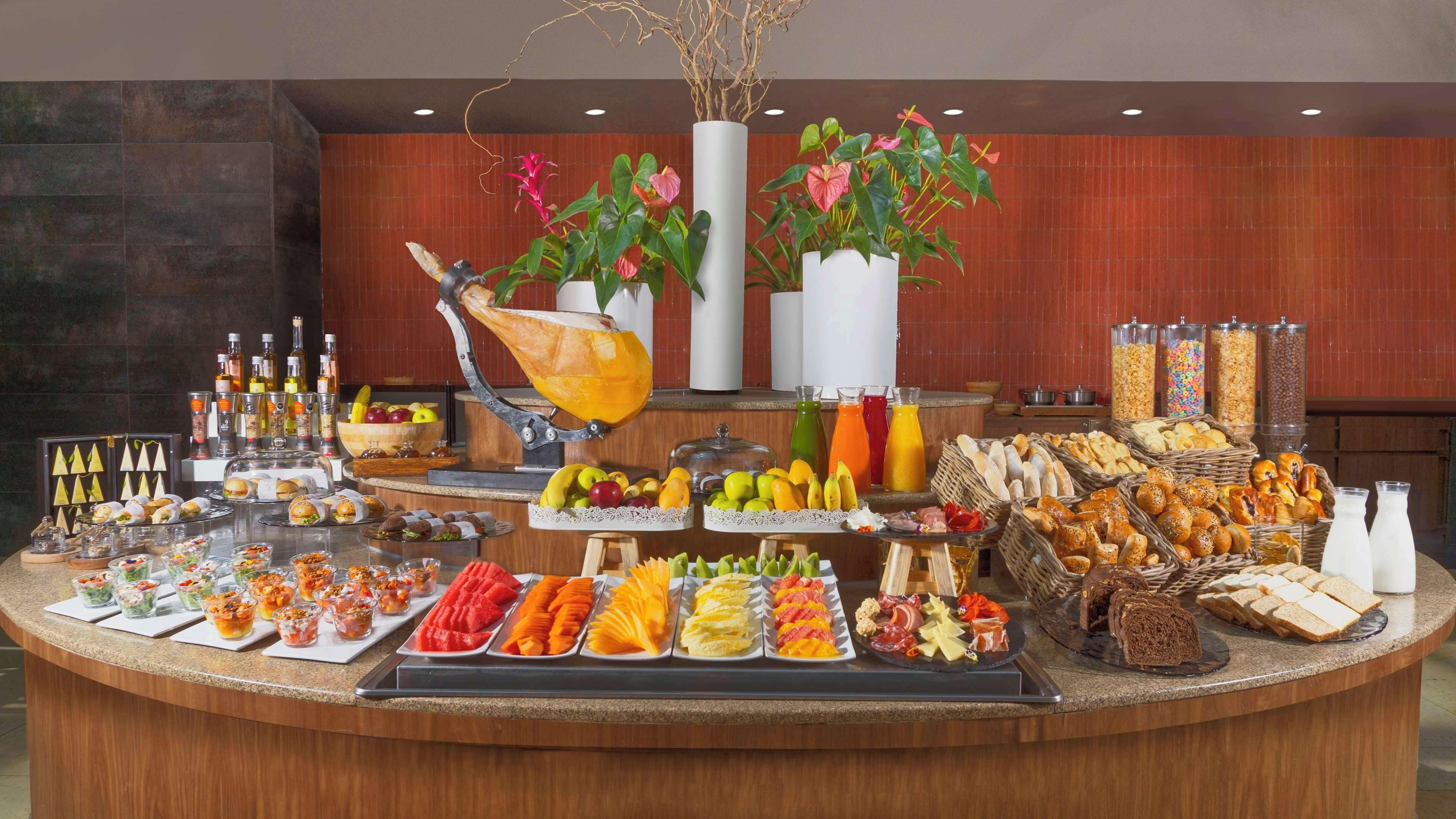 A buffet with various food items, drinks, and decorative plants.