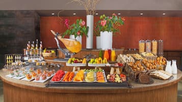 A buffet with various food items, drinks, and decorative plants.