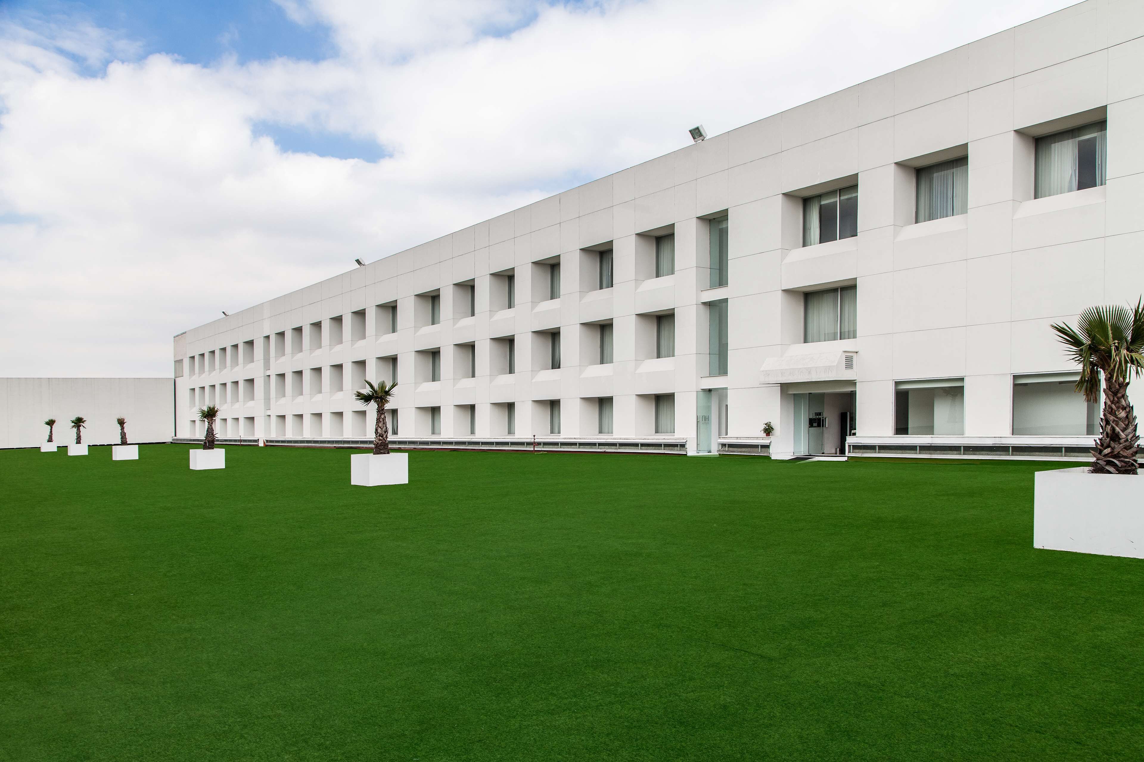 A modern building with a flat facade, multiple windows, and a green lawn with potted plants.
