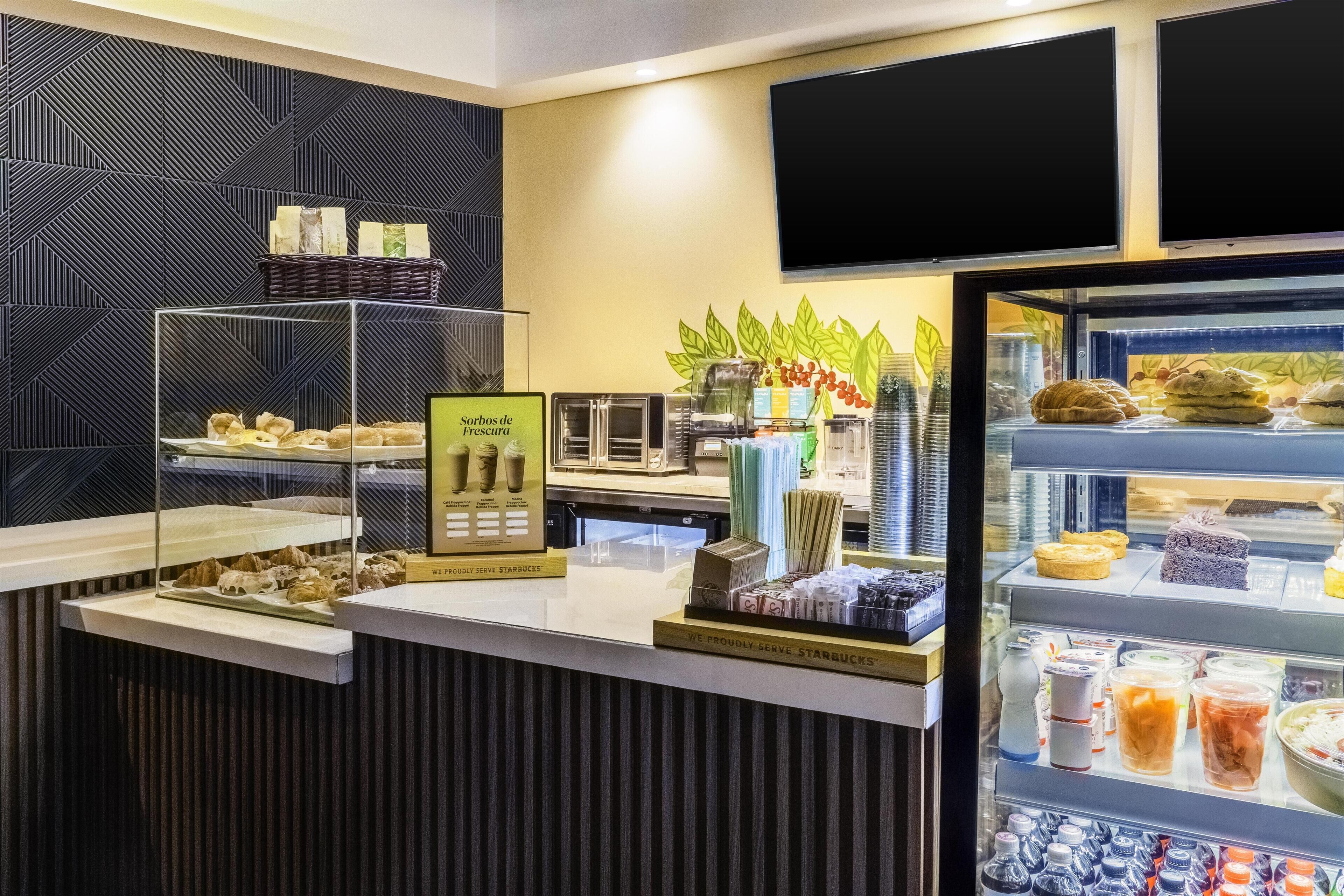 Mostrador de cafetería con pasteles, un tablero de menú y una exhibición de bebidas embotelladas.