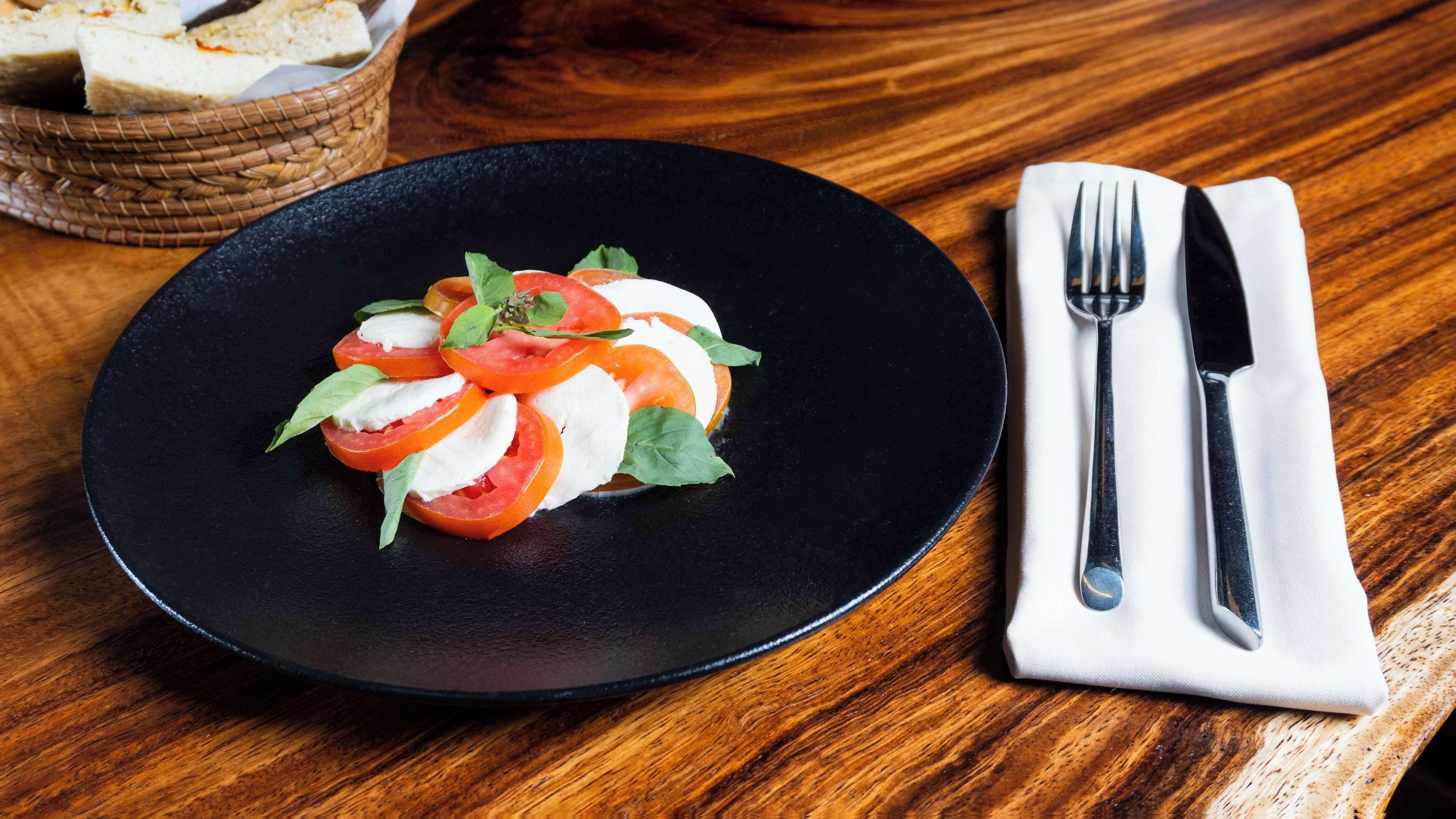 Plato negro con ensalada de tomate y mozzarella sobre una mesa de madera.