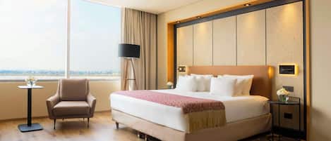 Habitación de hotel con una cama grande, una silla, una mesita con un florero y vistas a la ciudad.