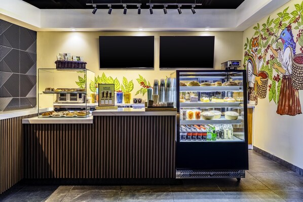 Un café avec un comptoir où sont exposées des pâtisseries et un réfrigérateur vitré contenant des boissons.