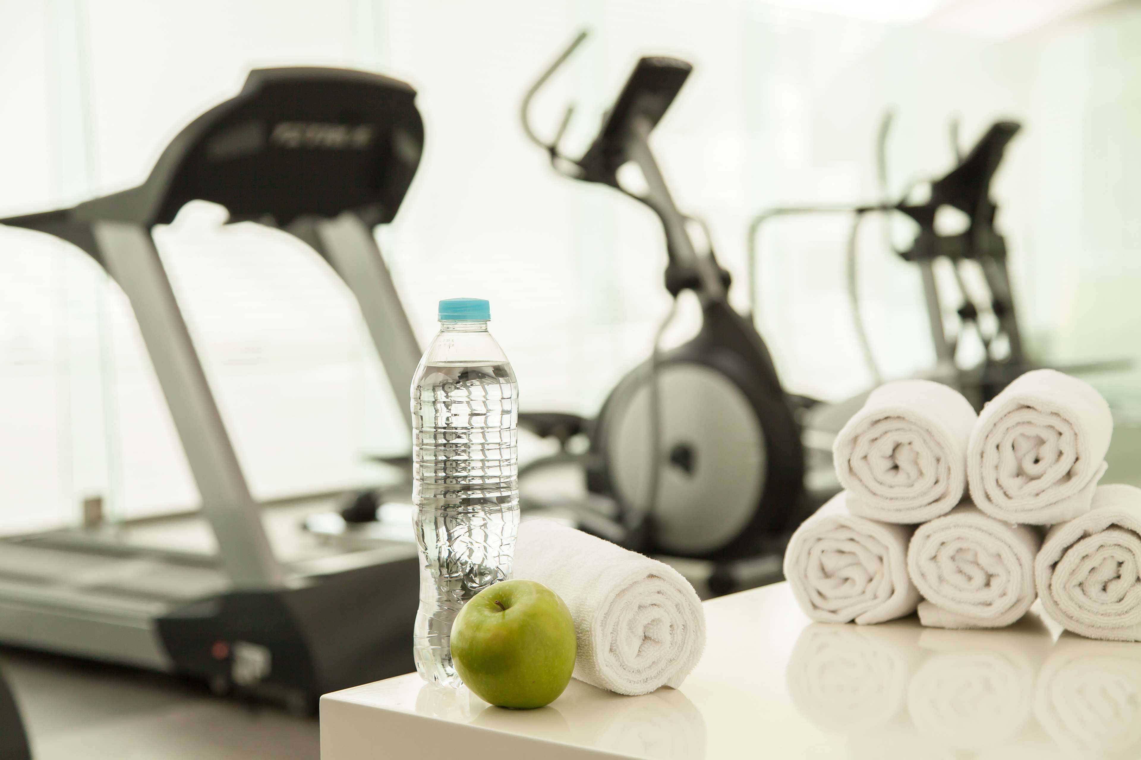 Ein Laufband, eine Wasserflasche und aufgerollte Handtücher auf einem Tisch.