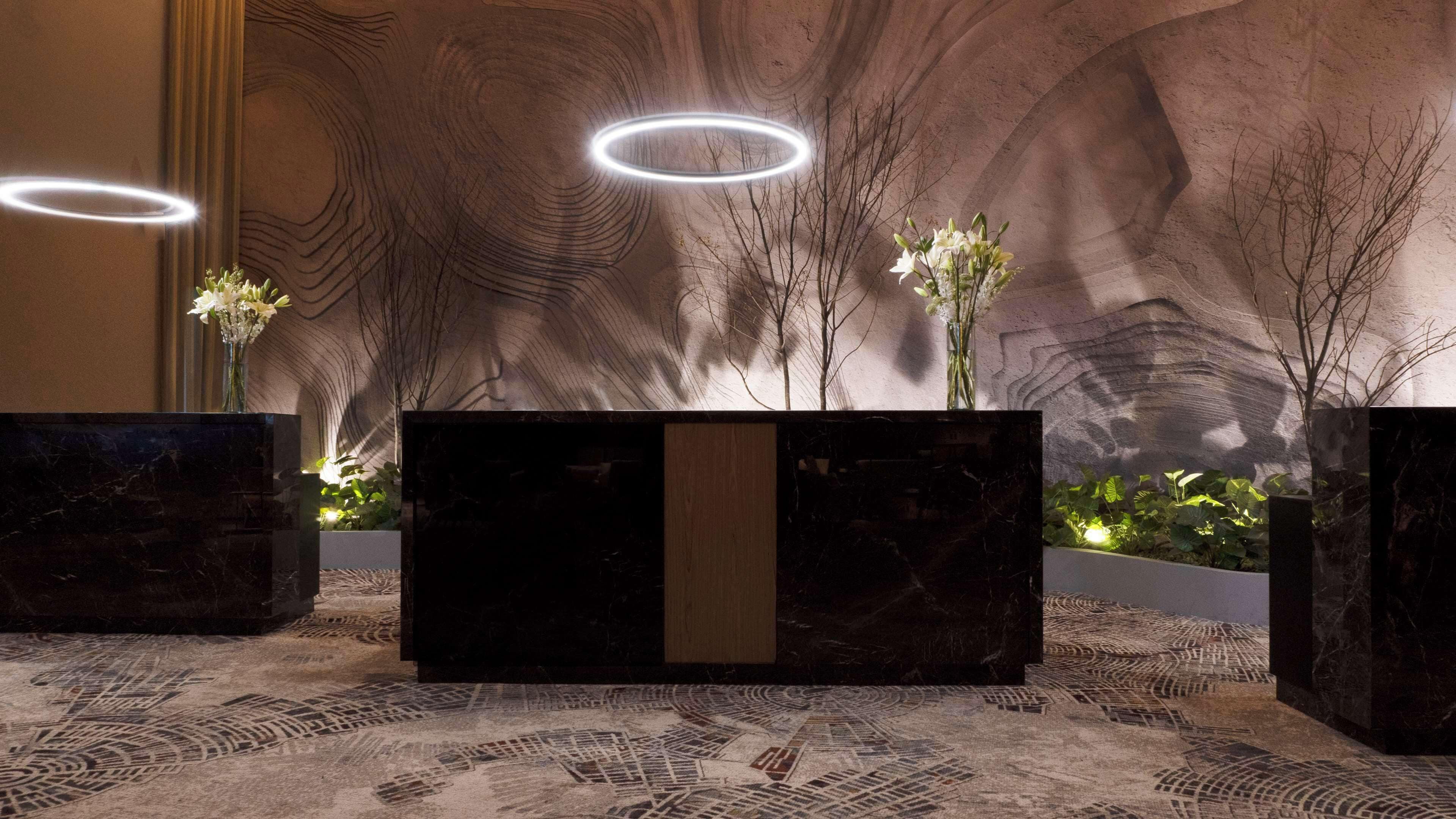 Un área de recepción con un mostrador de mármol, una alfombra estampada y una pared con diseño de vetas de madera.