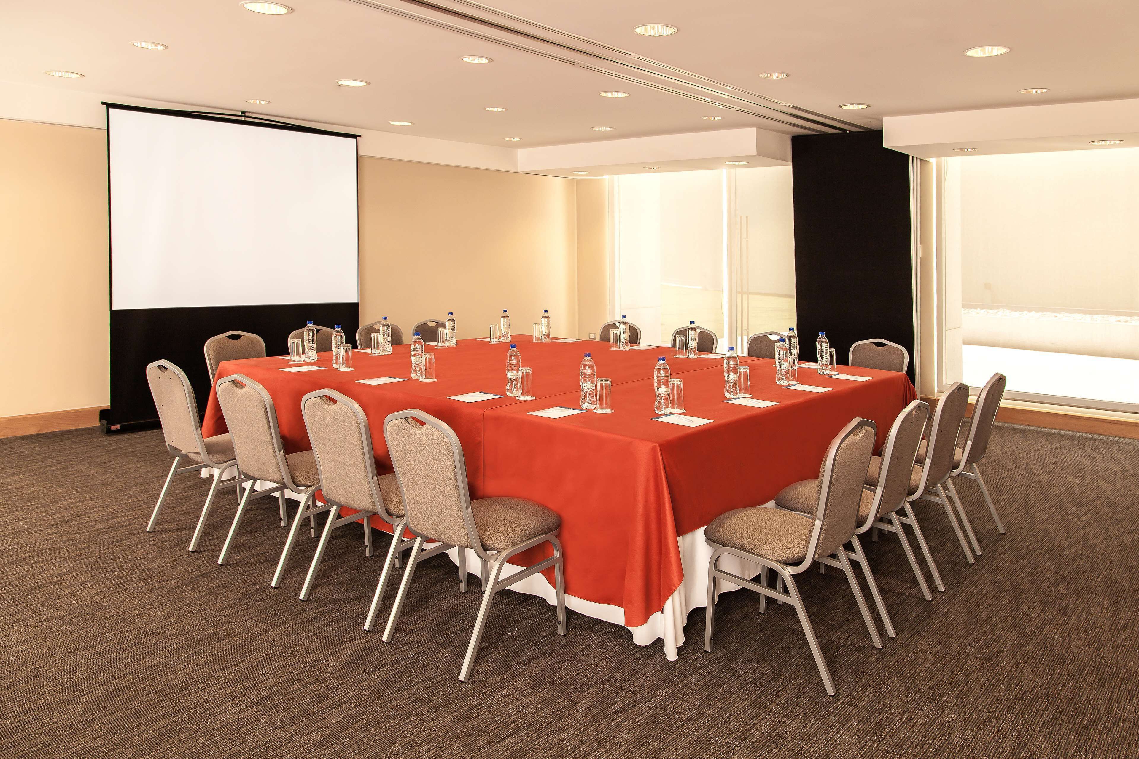 Une salle de conférence avec une longue table, des chaises, un écran de projection et une grande fenêtre.