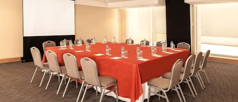A conference room with a long table, chairs, a projector screen, and a large window.