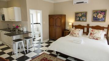 Una habitación de hotel con piso a cuadros, una cama con almohadas estampadas, un armario de madera, una cocina con gabinetes blancos y una alfombra roja.