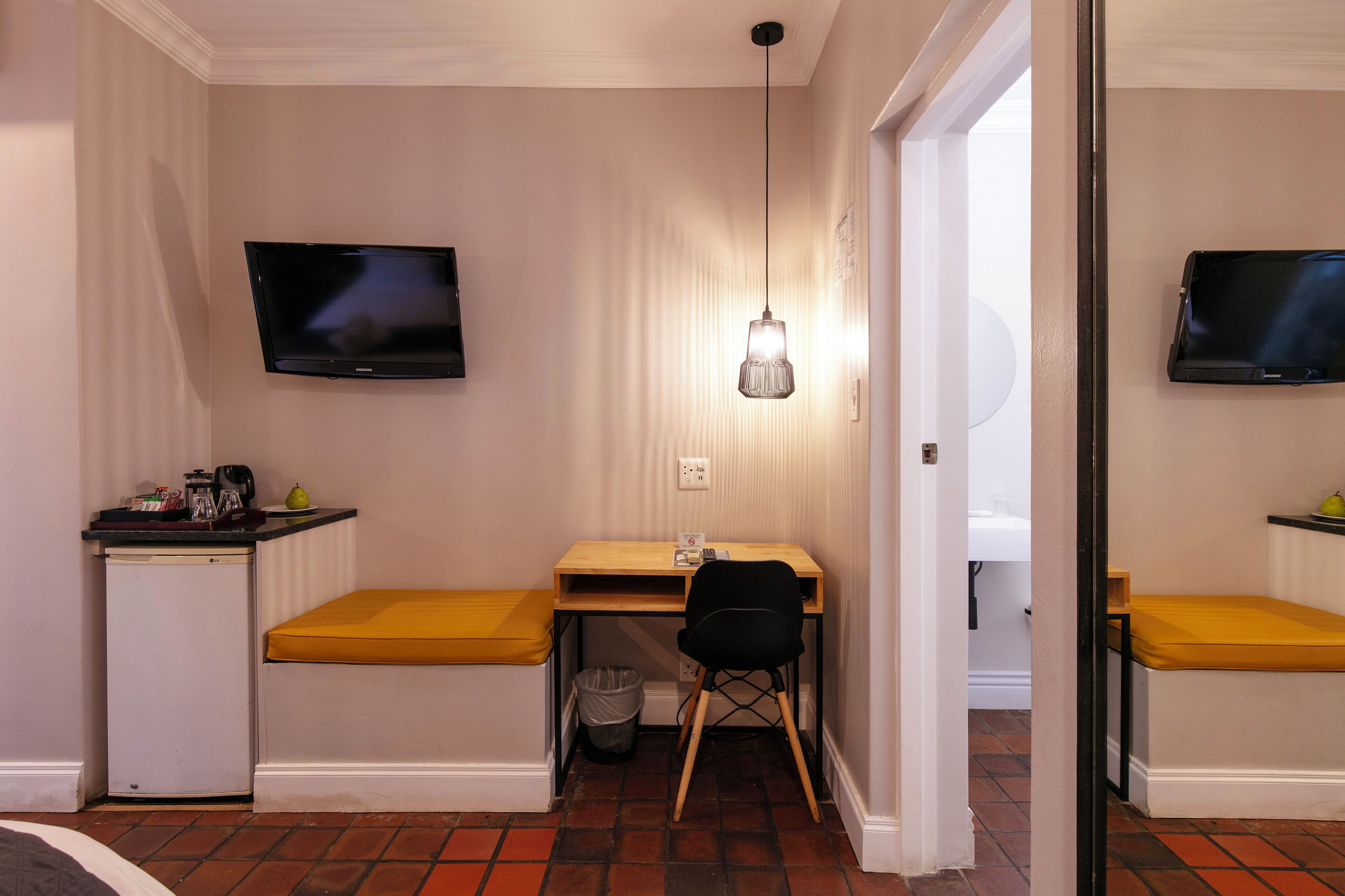 Habitación compacta con escritorio, silla, refrigerador pequeño y televisor montado en la pared.