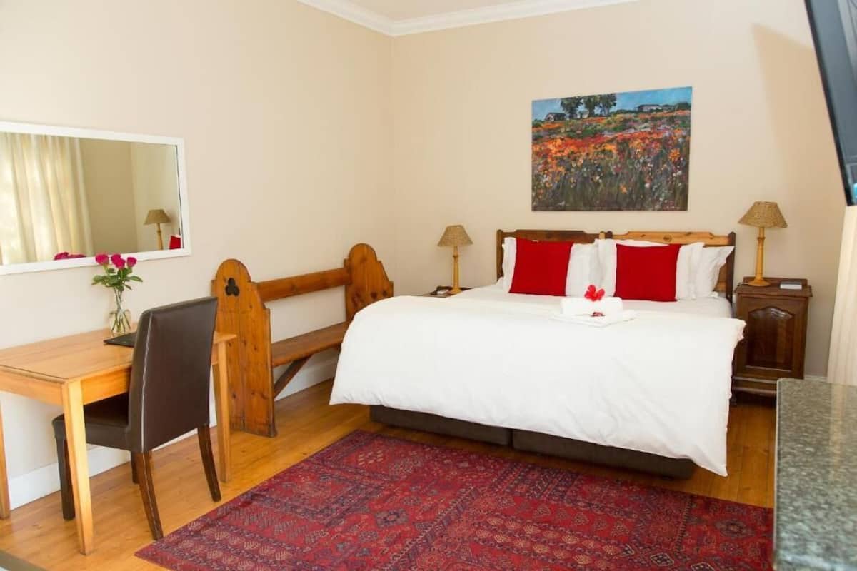 A bedroom with a wooden bed, a desk, a chair, a red rug, and a painting on the wall.