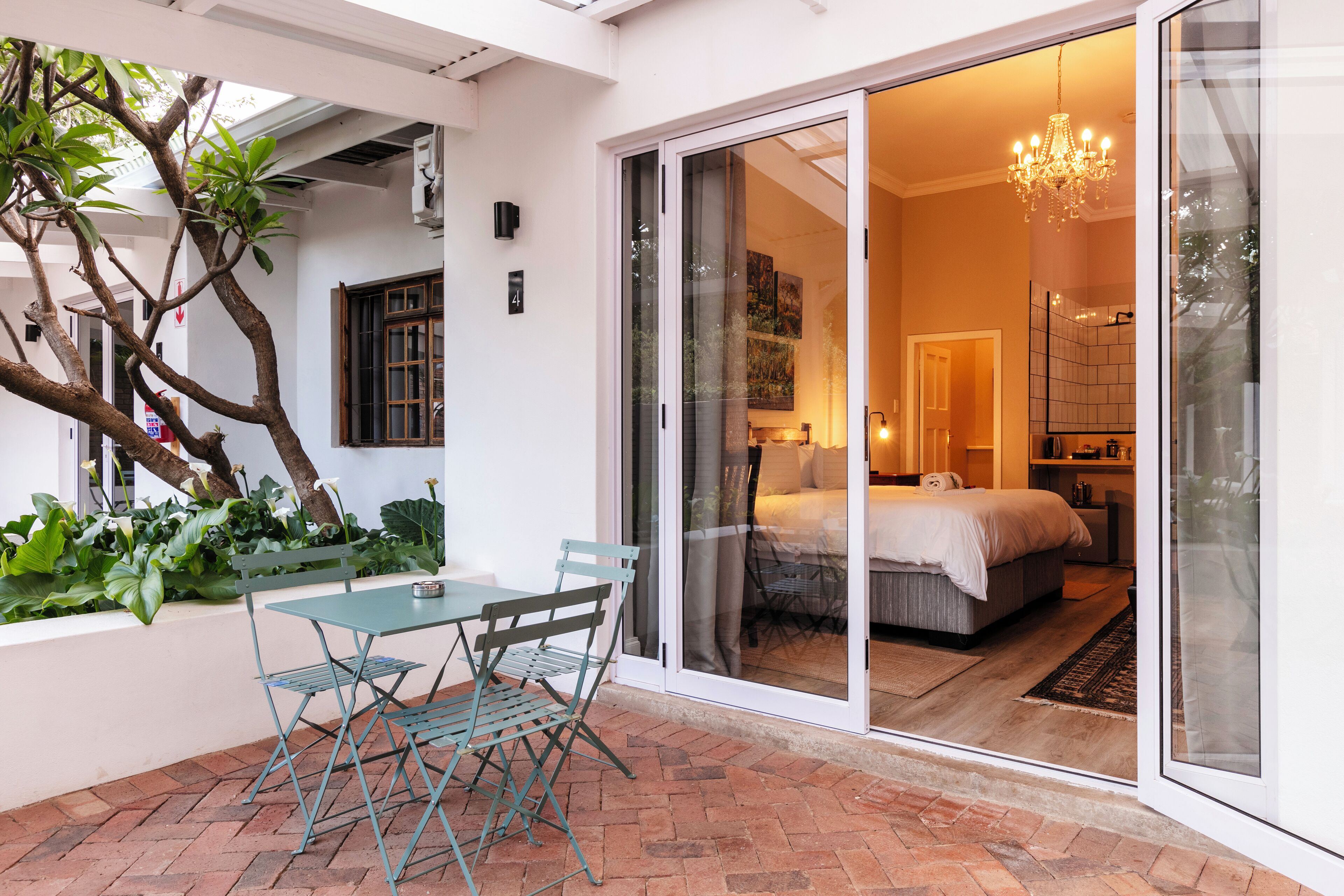 A modern hotel room with a sliding glass door leading to a balcony, a bed, a bedside table, and a chandelier.
