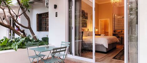 A modern hotel room with a sliding glass door leading to a balcony, a bed, a bedside table, and a chandelier.