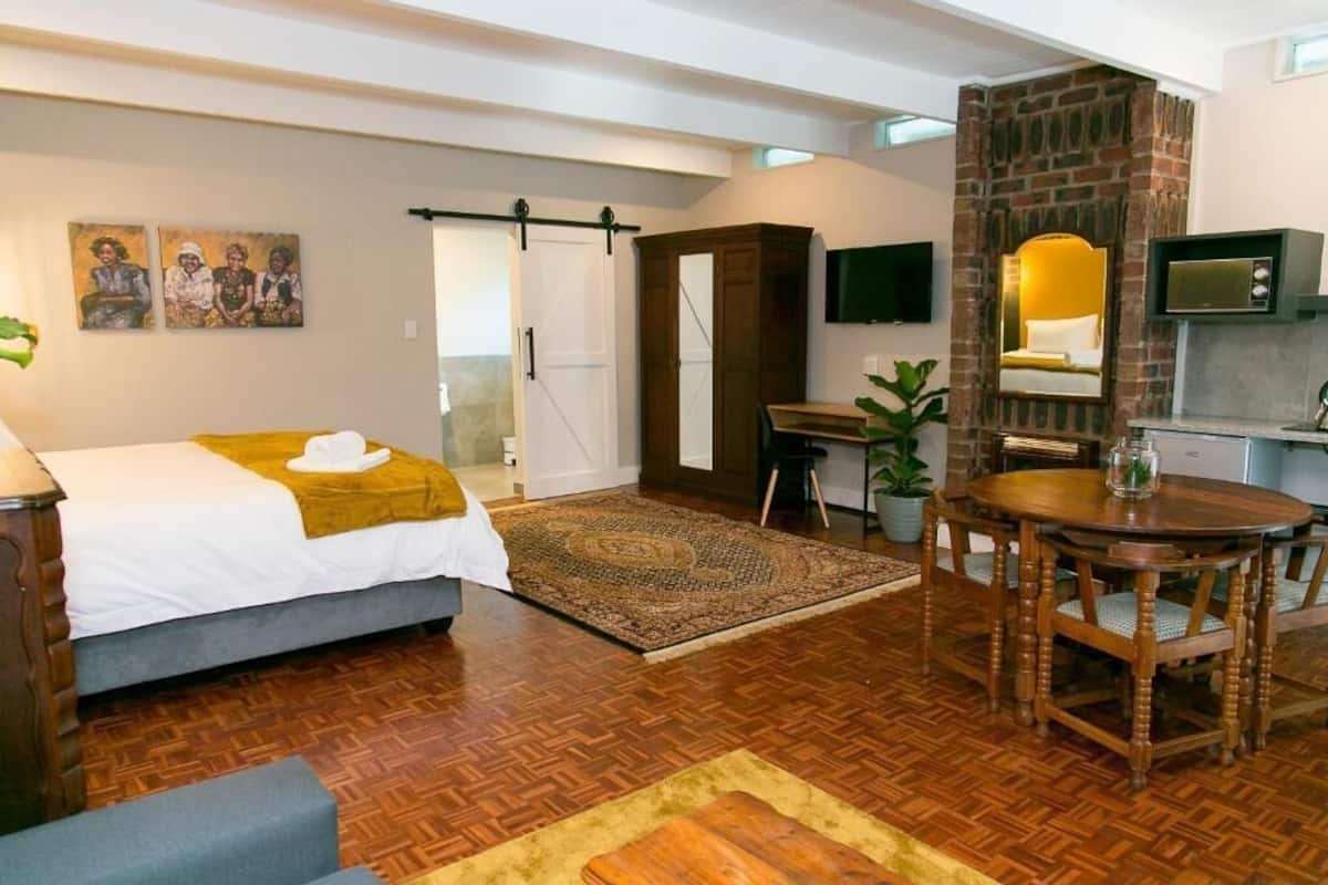 A bedroom with a bed, a desk, a dining table, a TV, and a fireplace.