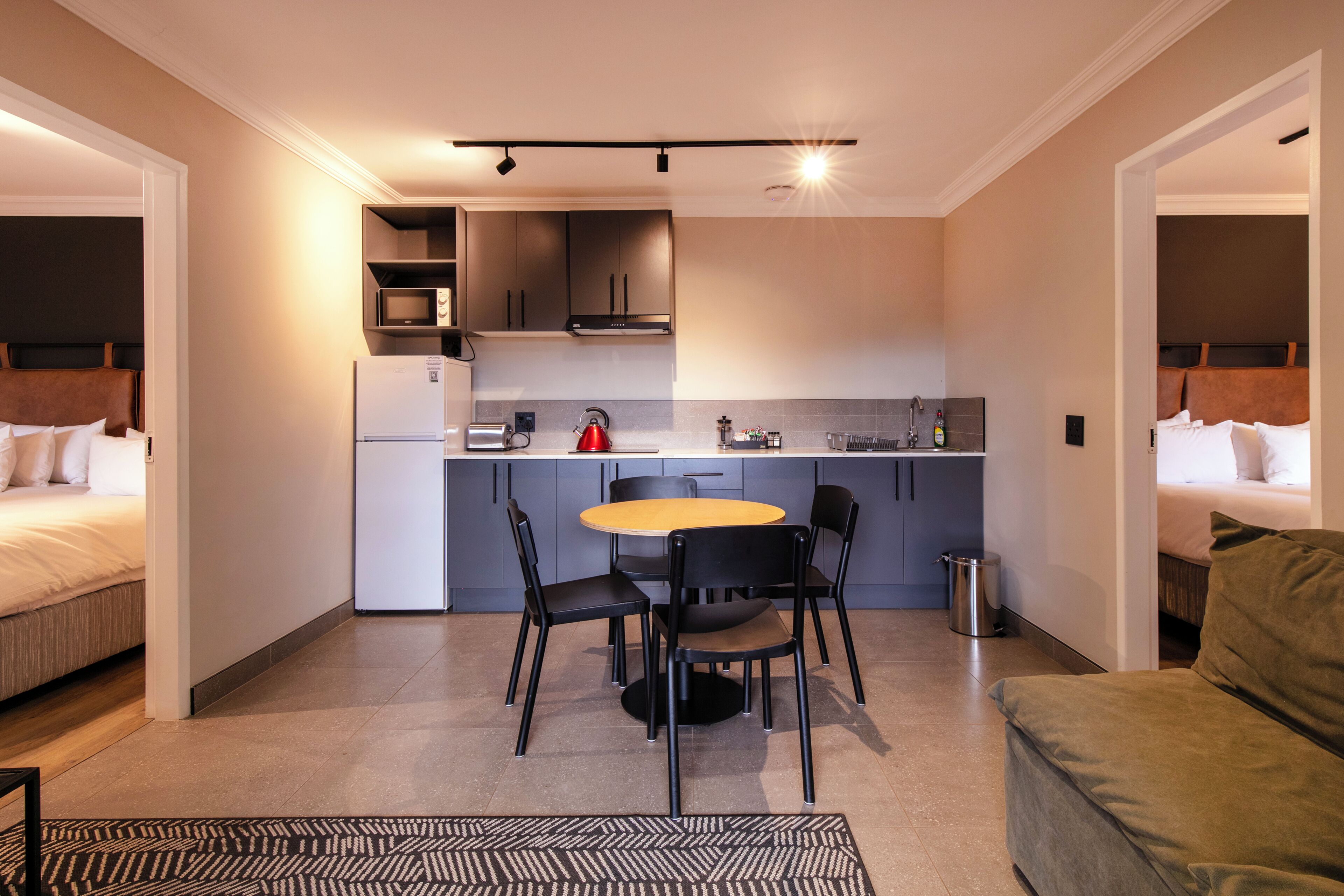 A compact hotel room with a kitchenette, a dining area, and a bed.