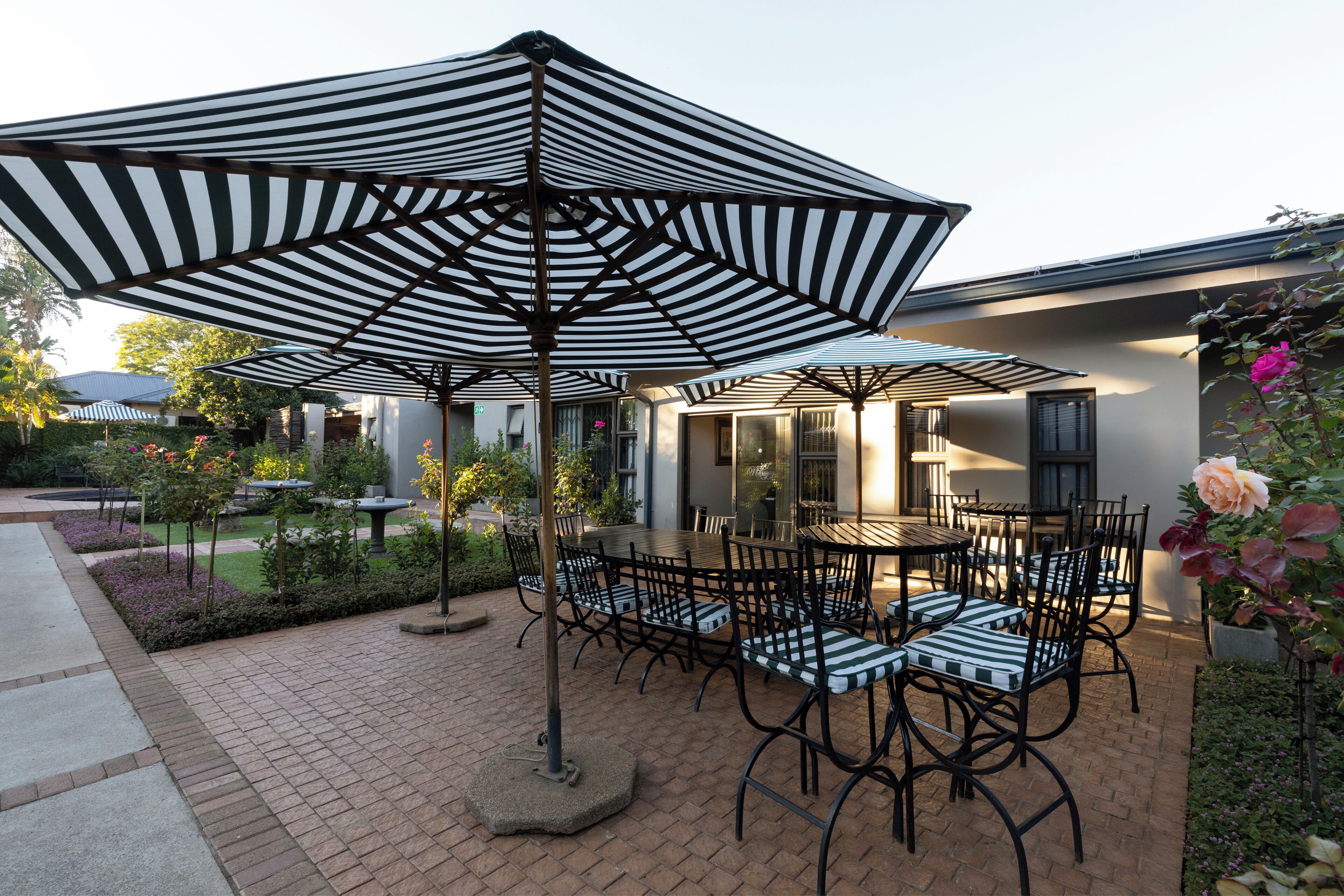 A patio area with tables and chairs, surrounded by a brick walkway and greenery.
