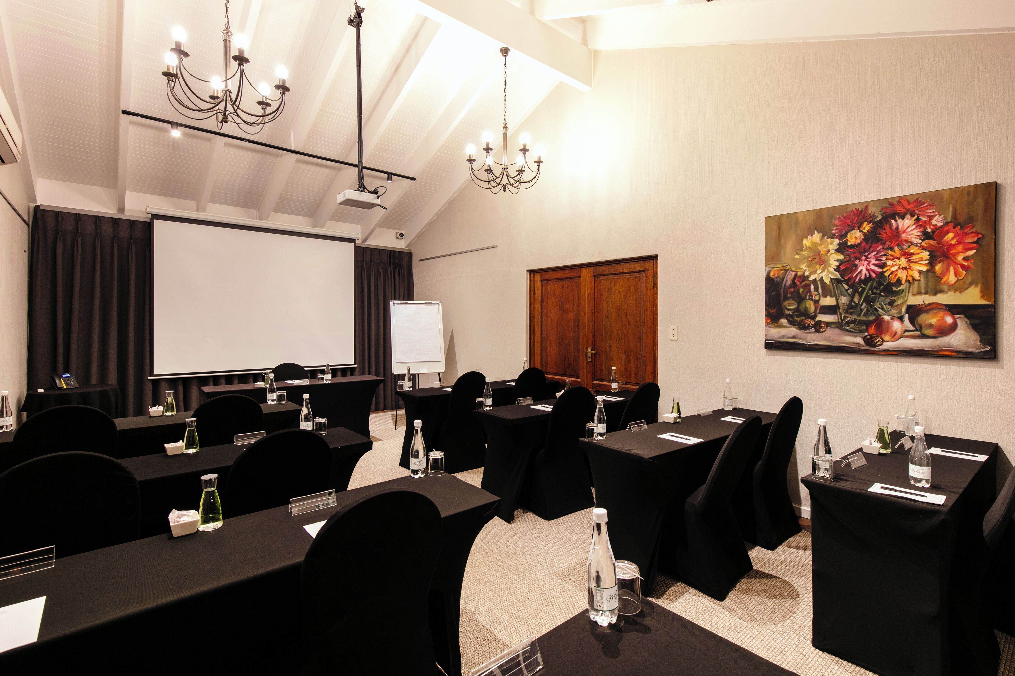 Uma sala de conferências com mesas, cadeiras, uma tela de projeção e um quadro na parede.