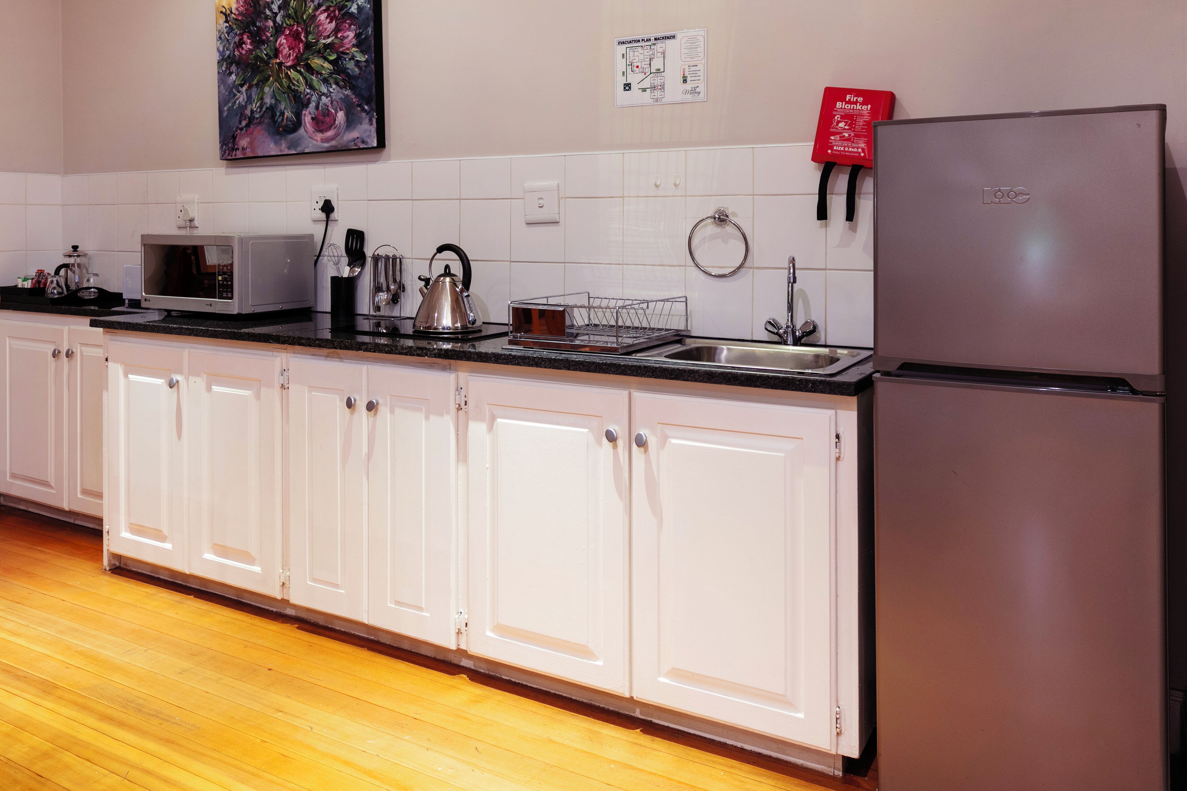 A kitchen with white cabinets, a microwave, a kettle, a sink, and a refrigerator.