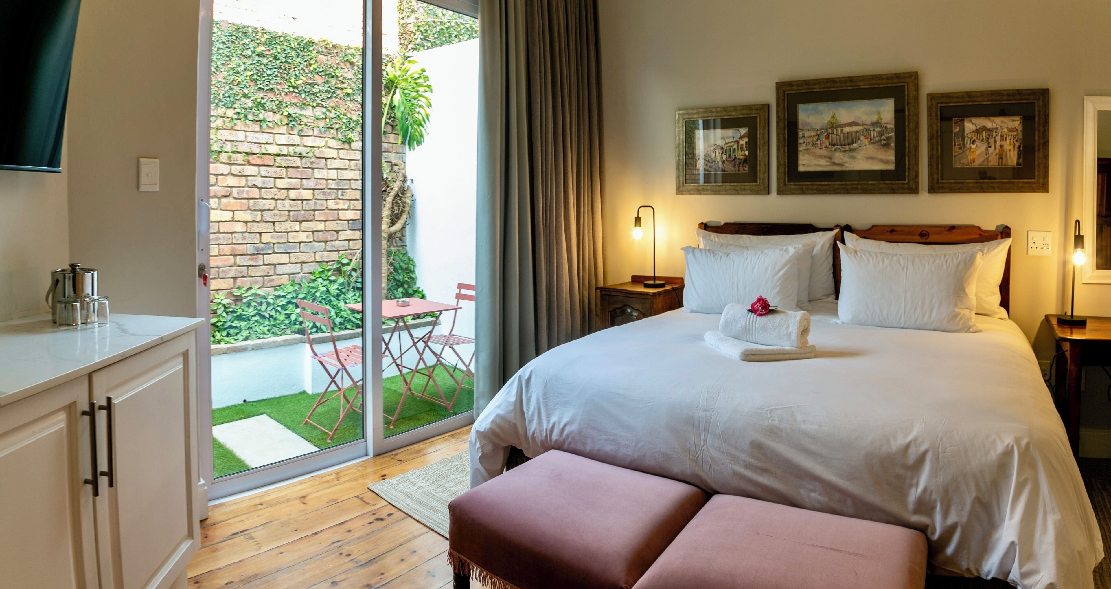 Ein Hotelzimmer mit Bett, Schreibtisch, Stuhl, kleinem Tisch und Blick auf eine Ziegelwand und Grünfläche draußen.
