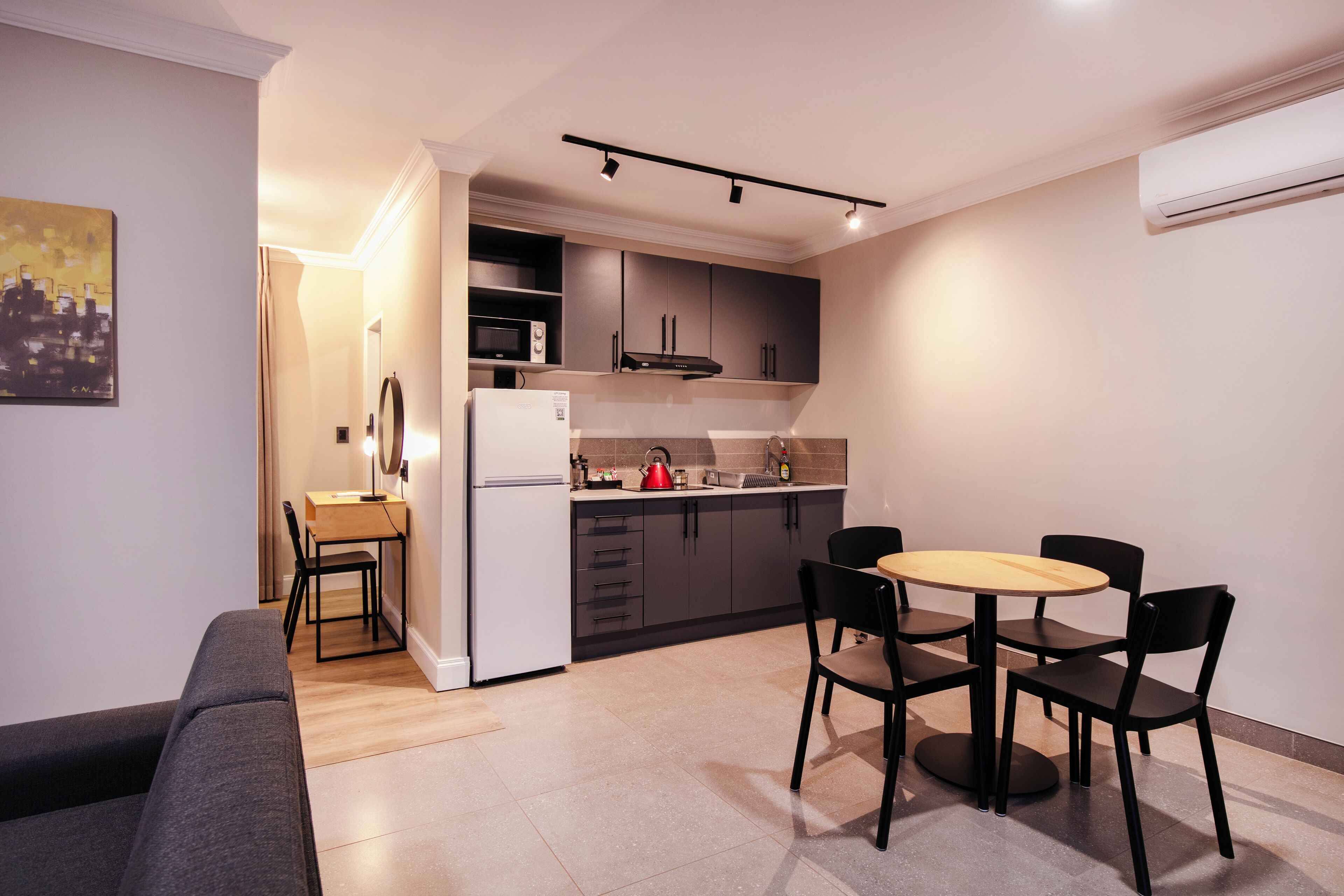 Cozinha compacta com área de refeições, incluindo geladeira, micro-ondas e uma pequena mesa com cadeiras.