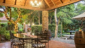 An outdoor patio with a round table and chairs, surrounded by greenery and a brick pillar. - Murray Street 137 Guest House (Pretoria)