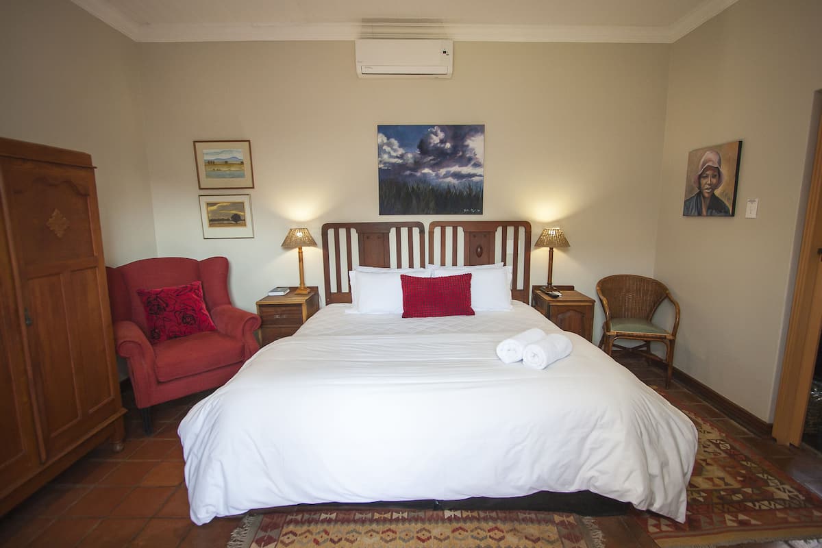 A hotel room with a large bed, a red armchair, two nightstands with lamps, a wooden wardrobe, and a painting on the wall.