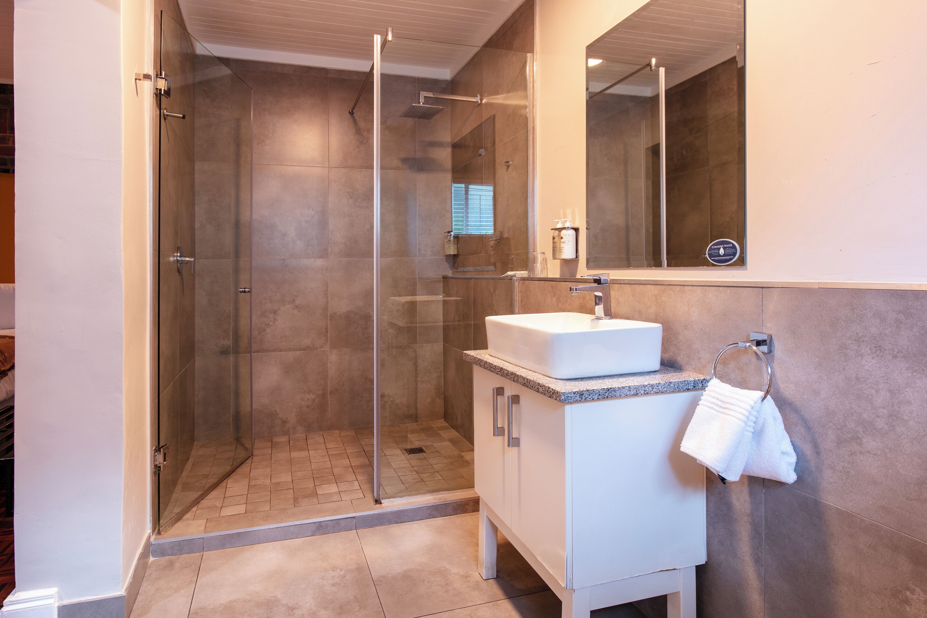 A modern bathroom with a glass-enclosed shower, a white sink, and a mirror above it.