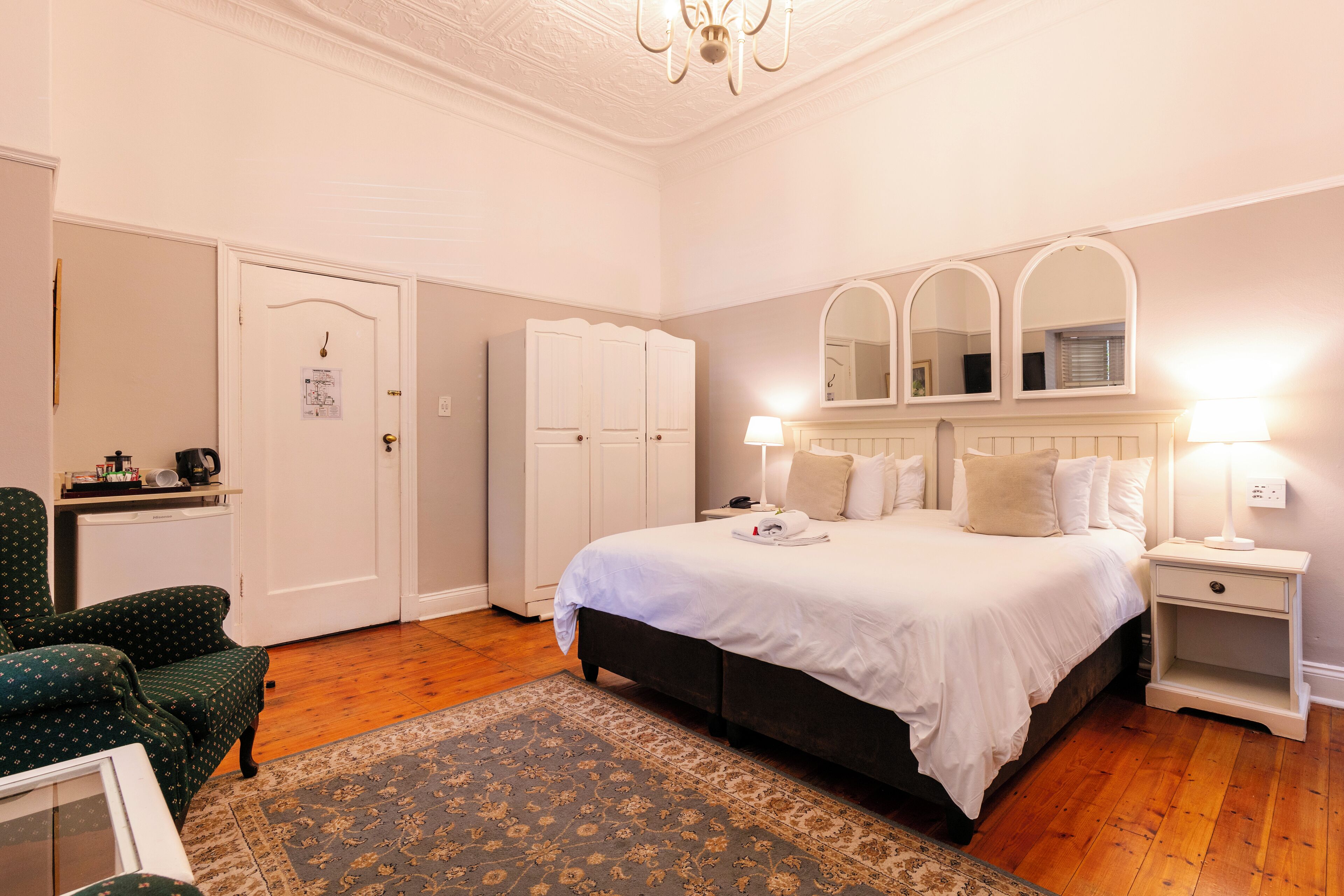 A bedroom with a large bed, two bedside tables with lamps, a chair, a wardrobe, and a door.