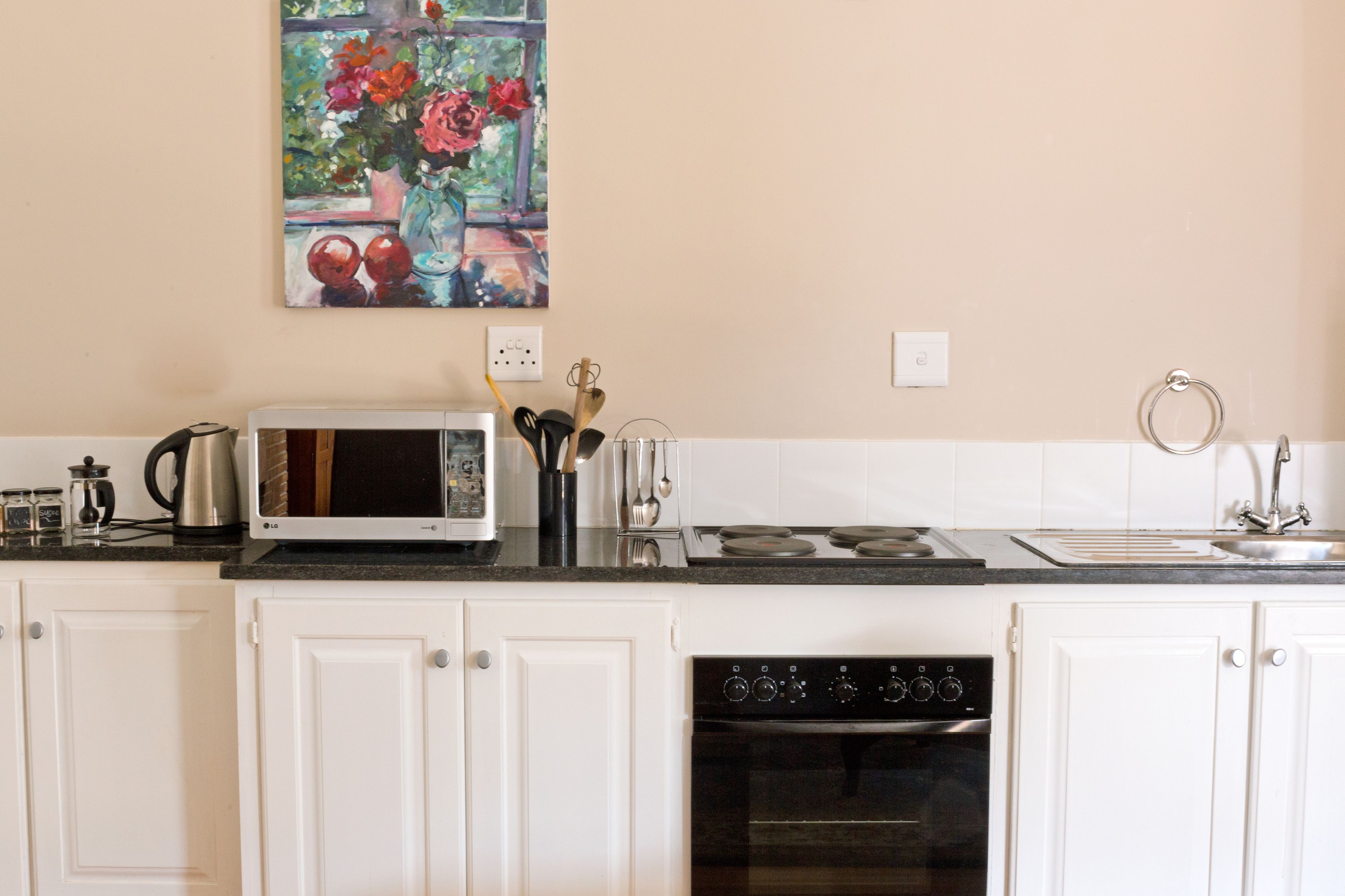 A kitchen with white cabinets, a microwave, stove, and oven. There is a painting on the wall above the counter.