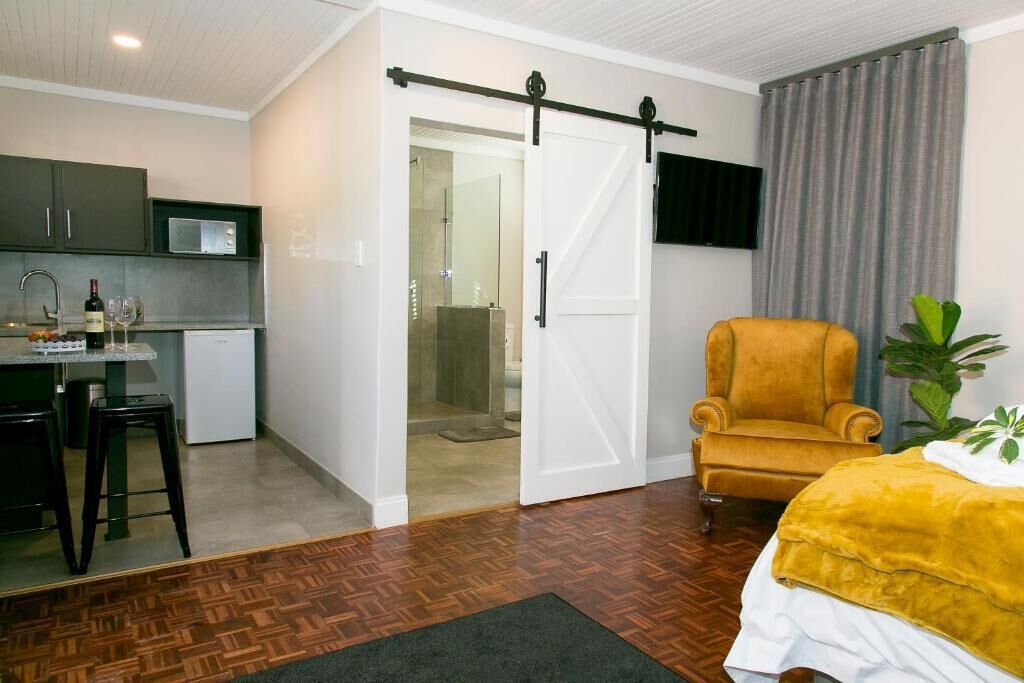 Une chambre d’hôtel compacte comprenant un coin cuisine, une porte coulissante donnant accès à la salle de bain, un fauteuil jaune et un lit avec une couverture jaune.
