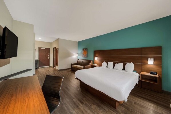 A hotel room with a large bed, a desk, a chair, a TV, and a wooden floor.
