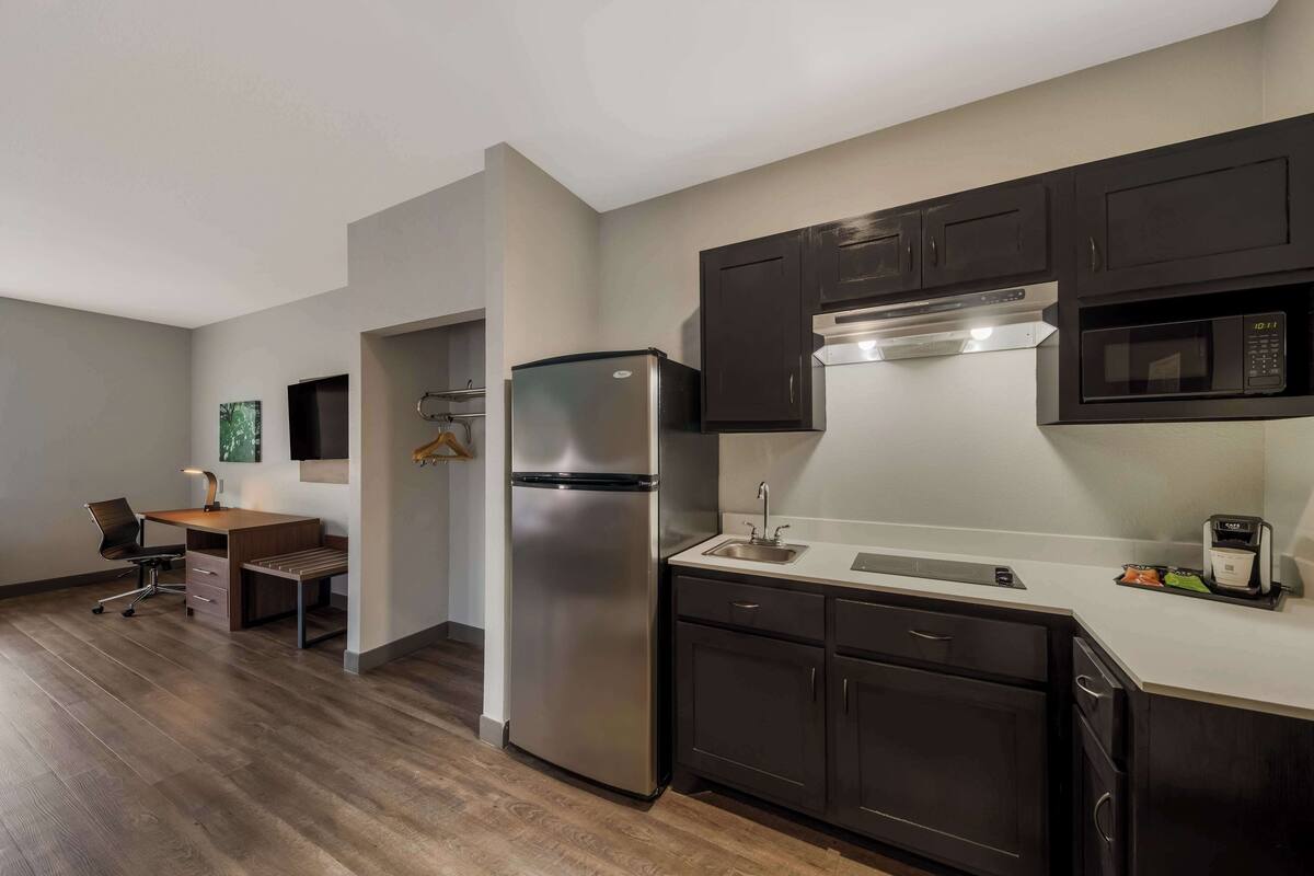 A modern kitchen with dark cabinets, a stainless steel refrigerator, a microwave, and a coffee maker.