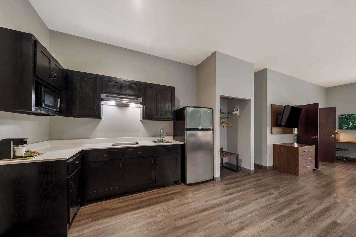 A modern kitchen with dark cabinets, a stainless steel refrigerator, and a white countertop.