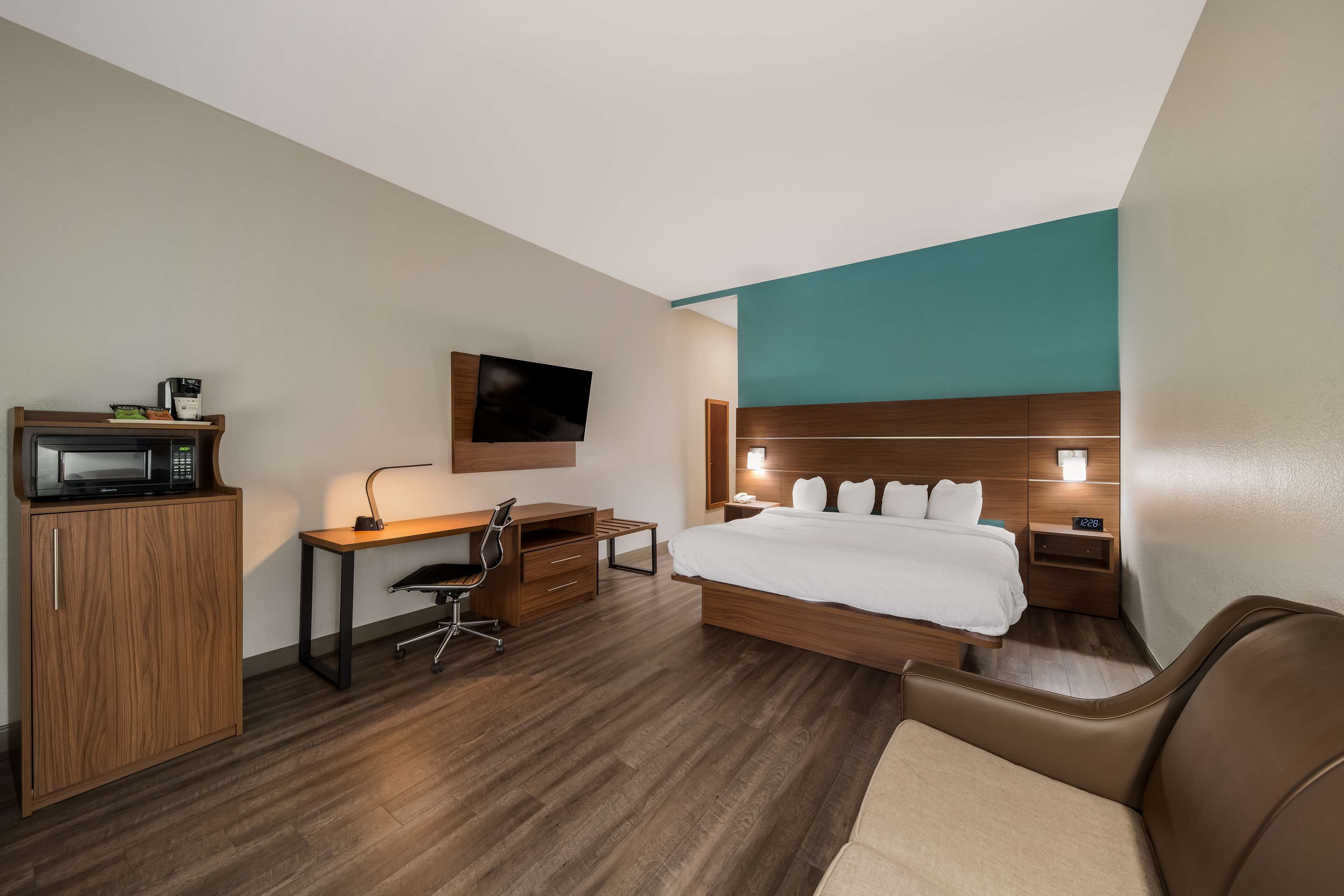 A hotel room with a bed, desk, chair, TV, and a microwave.