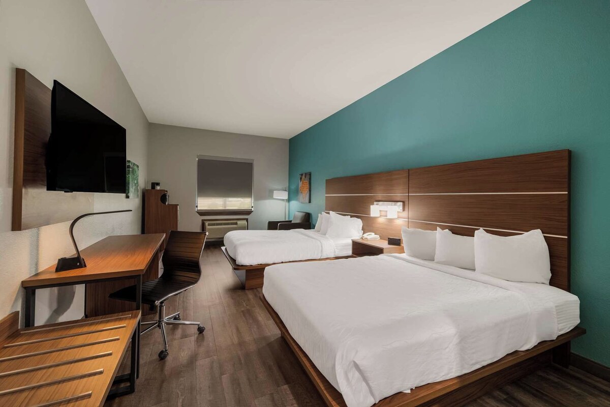 A hotel room with two beds, a desk, a chair, a flat-screen TV, and a window.
