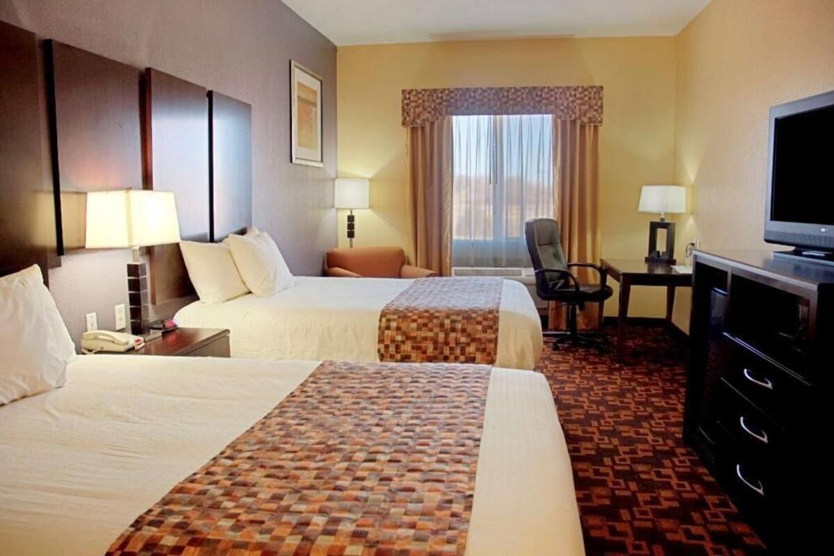 A hotel room with two beds, a desk with a chair, a television, and a telephone.