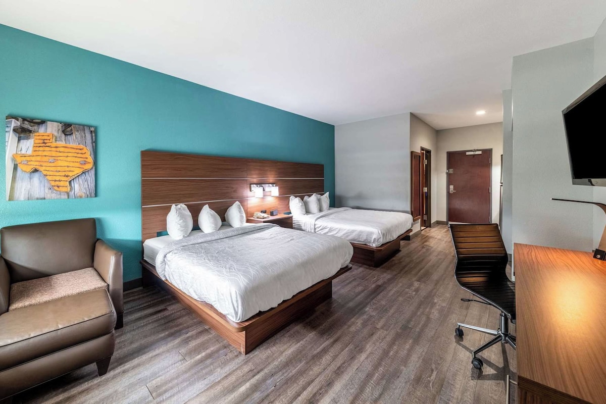 A hotel room with two beds, a desk, a chair, and a television.