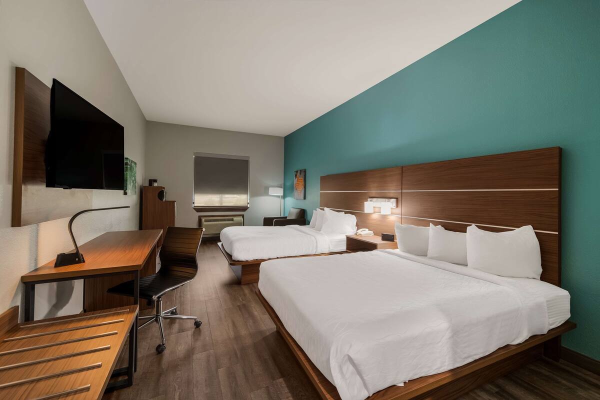 A hotel room with two beds, a desk, a chair, a TV, and a nightstand.