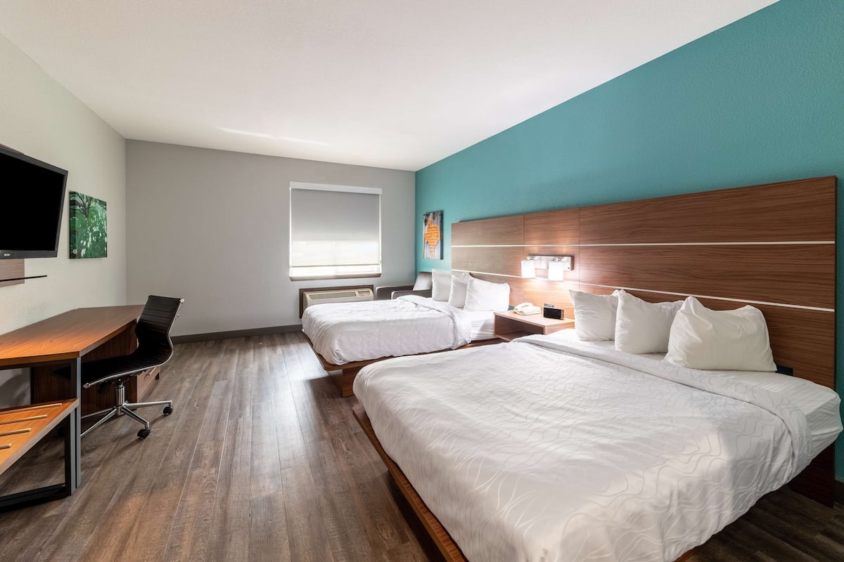 A hotel room with two beds, a desk, a chair, a TV, and a window.