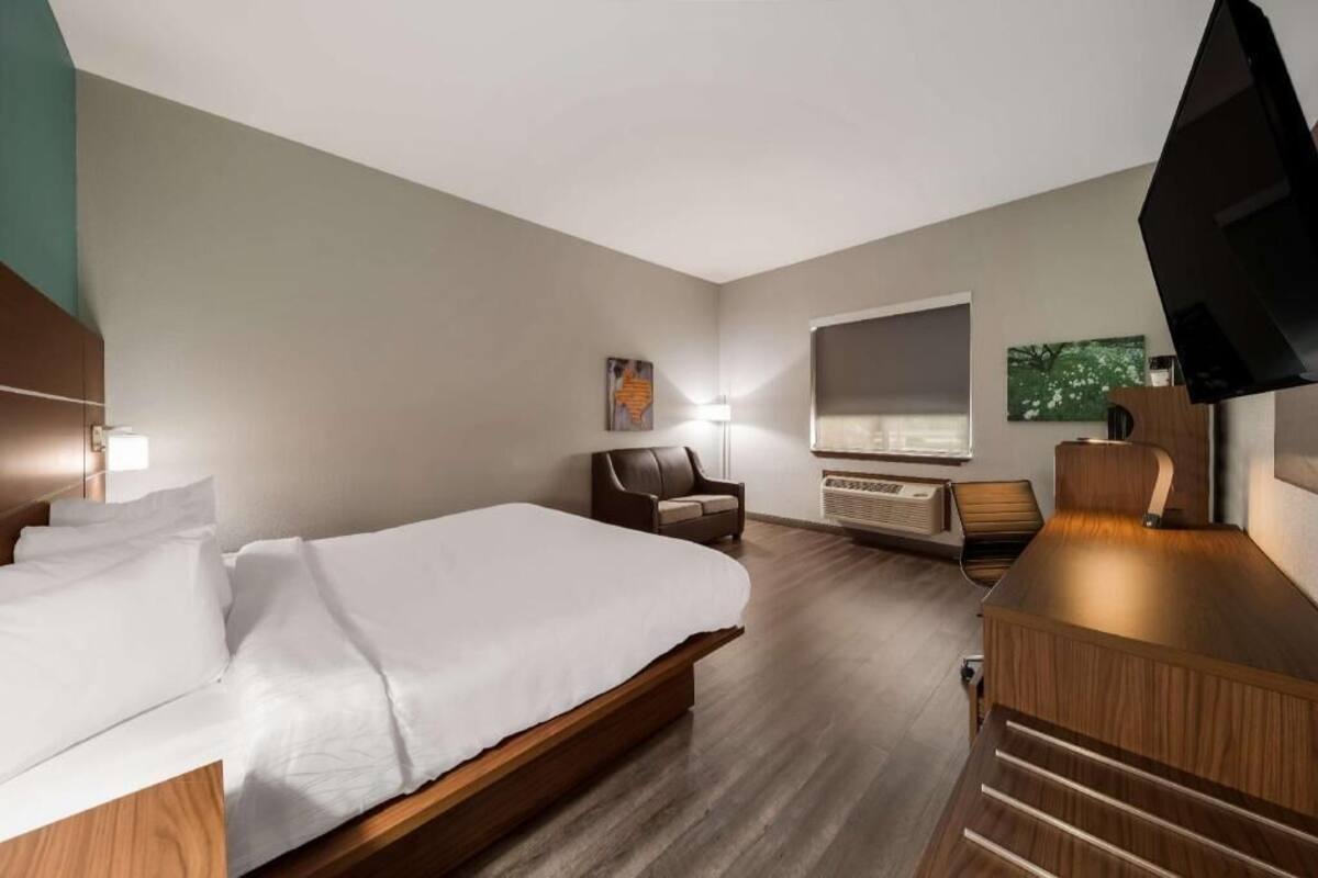 A hotel room with a bed, a desk, a chair, a television, and a window.