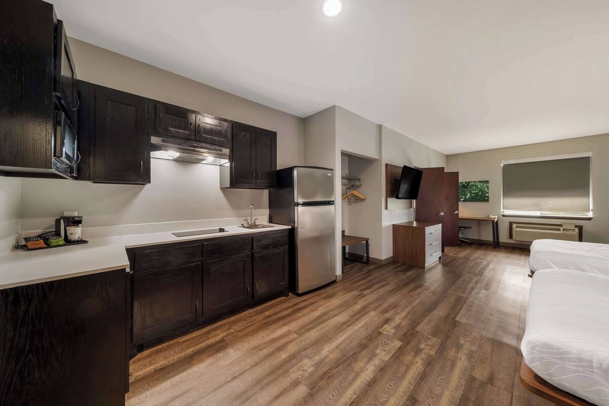 A compact kitchen with dark cabinets, a stainless steel refrigerator, and a white countertop.