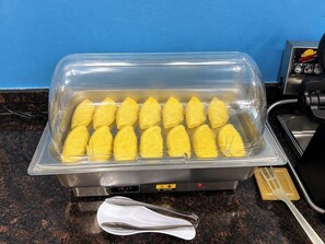 A buffet setup with a clear plastic container holding food items, a digital temperature display, and a caution sign.