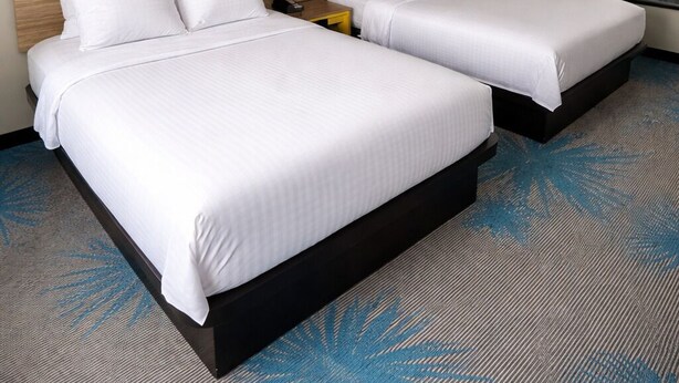 A hotel room with two beds, a nightstand, a wall-mounted phone, and a large sunset painting. - Days Inn by Wyndham Lincoln, IL/Route 66 (Lincoln)