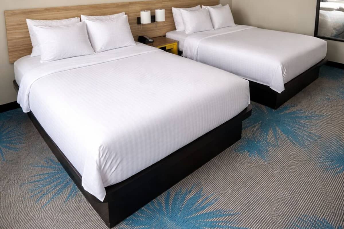 A hotel room with two beds, a nightstand, a wall-mounted phone, and a large sunset painting.