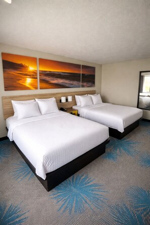 A hotel room with two beds, a nightstand, a wall-mounted phone, and a large sunset painting.