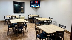 A conference room with multiple tables and chairs, a large flat-screen TV mounted on the wall, and a window with a view of a vehicle outside. - Days Inn by Wyndham Lincoln, IL/Route 66 (Lincoln)