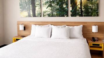 A hotel room with a large bed, a headboard with a light fixture, and a wall-mounted artwork of a forest scene.